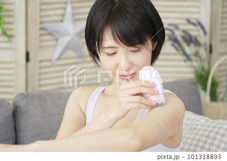リビングで家庭用脱毛器で腕のセルフ脱毛をする女性 101318893