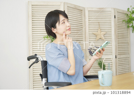 リビングでスマートフォンを使いながら想像する車椅子に乗った女性 101318894