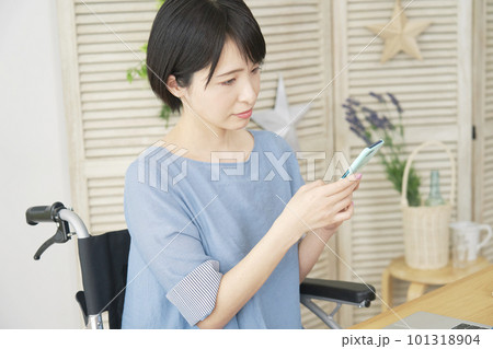 リビングでスマートフォンを使う車椅子に乗った女性 101318904