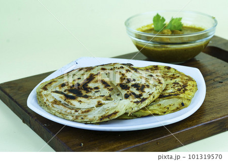 roti canai and curry sauce in white plate with served on the wooden chopping board. 101319570