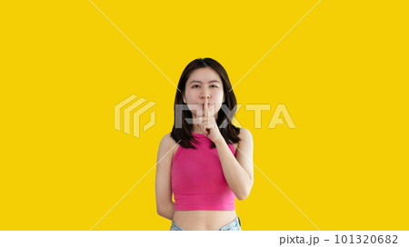 Asian woman doing silent gesture with finger, Noiseless signal transmission, Noiseless symbol, Hide a secret, Crossed hands, Do not speak, Shut your mouth, Isolated on yellow background . 101320682