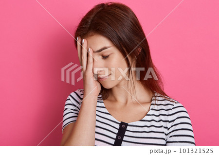 Tired young woman covers face with palm, closes her eyes, feels exhausted, wearing casual striped t shirt, posing isolated over pink background, wants to sleep. Tired young woman covers face with palm, closes her eyes, feels exhausted, wearing casual striped t shirt, posing isolated over pink background, wants to sleep. 101321525