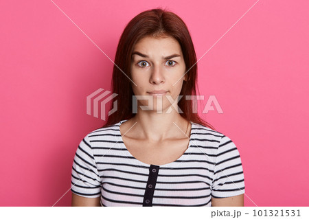 Misunderstanding lady looking directly at camera, wearing casual striped t shirt, posing isolated over pink background, looks at camera with serious look. Misunderstanding lady looking directly at camera, wearing casual striped t shirt, posing isolated over pink background, looks at camera with serious look. 101321531