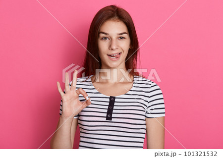 Young beautiful woman doing ok sign with fingers and showing her tounge, looking directly at camera with funny expression, posing isolated over pink background. Young beautiful woman doing ok sign with fingers and showing her tounge, looking directly at camera with funny expression, posing isolated over pink background. 101321532