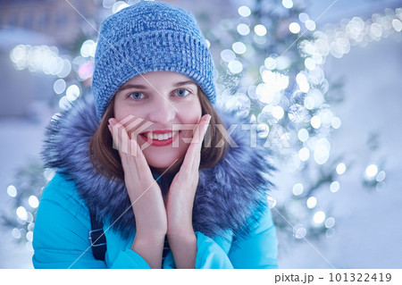 Outdoor photo of young beautiful female walks on street, wears stylish winter clothes, admires magic lights, has pleased expression, shining smile and red lips. Christmas and New Year concept 101322419