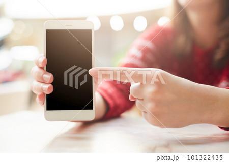 Selective focus. Unrecognizable female keeps modern white smart phone in hand, points with finger at blank copy screen for your text or information content. Technology and communication concept 101322435