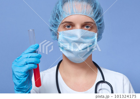 Closeup portrait of physician carrying blood tube in hands, doctor with stethoscope over neck, dresses disposable hat, medical mask and gloves. Laboratory employe makes blood test. Health care concept 101324175