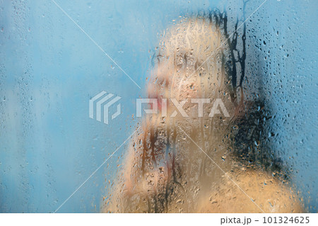 Indoor shot of beautiful young female with wet hair and perfect slim body poses in shower cabine, takes douche, thinks about something as feels relaxation and relief. Hygiene and relax concept 101324625
