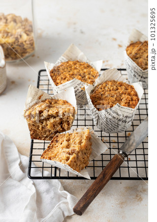 Morning breakfast oatmeal muffins in white paper cups on cooling rack with knife on white textured background Morning breakfast oatmeal muffins in white paper cups on cooling rack with knife on white textured background 101325695