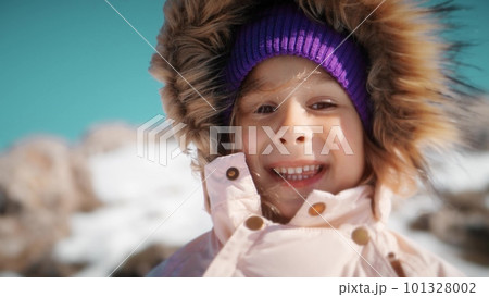 Close-up portrait of a beautiful little girl wearing warm clothes in snowy mountains in winter 101328002
