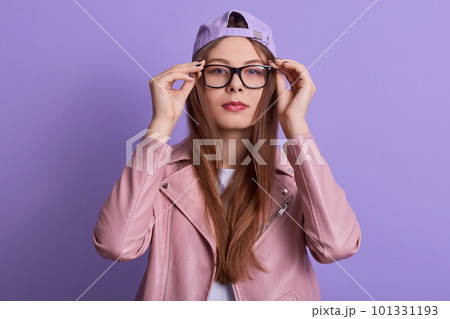 Close up portrait of concentrated serious young female touching eyeglasses frame with fingers, trying new eyewear, looking directly at camera, wearing stylish clothes. Youth and trend concept. Close up portrait of concentrated serious young female touching eyeglasses frame with fingers, trying new eyewear, looking directly at camera, wearing stylish clothes. Youth and trend concept. 101331193