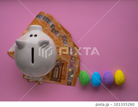Piggy bank surrounded by colorful Easter eggs on pink background. Piggy bank surrounded by colorful Easter eggs on pink background. 101335260