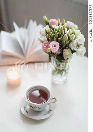 a spring still life, a bouquet of roses in a vase, a cup of tea and an book on white table. spring greeting card with spring flowers. Romantic background 101335577