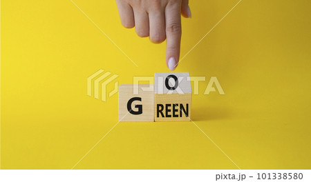 Go green symbol. Businessman hand points at turned wooden cubes with words Go Green. Beautiful yellow background. Ecological and Business and Go green concept. Copy space Go green symbol. Businessman hand points at turned wooden cubes with words Go Green. Beautiful yellow background. Ecological and Business and Go green concept. Copy space 101338580