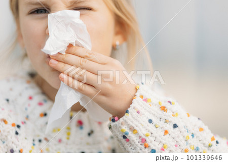 Close up up little girl's hand in white dotted sweater wiping her face with napkin outdoors 101339646