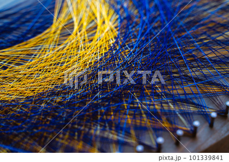 Colored thread mandala on a wooden board with nails. Mandala Moon Harmony Sun esotericism and psychology pictures from yellow and blue silk threads. 101339841