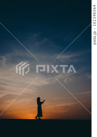 夕焼けに佇むシルエットの女性 101346564