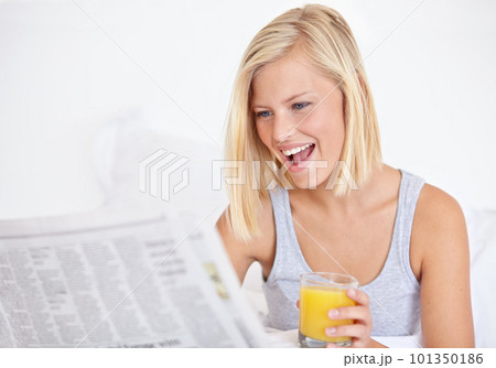 Catching up on her current affairs. A pretty young woman reading the newspaper in bed and enjoying a glass of OJ. 101350186
