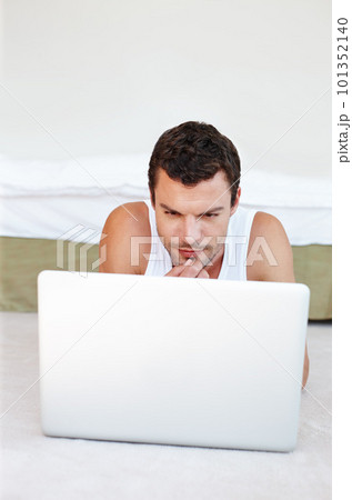 Its never too early to start blogging. A handsome man lying on his bed working on his laptop. 101352140