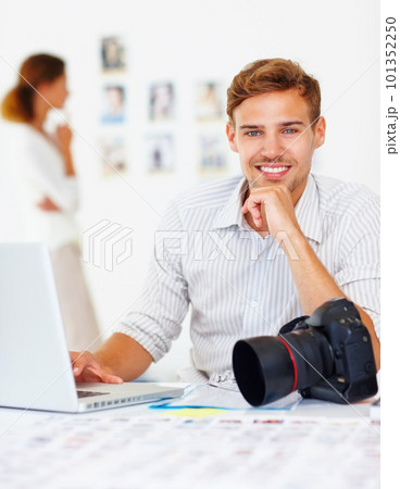 Young smiling photographer. Portrait of young smiling photographer using laptop with woman looking at images in background. 101352250
