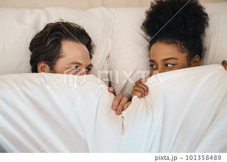 Interracial, happy and relaxed couple lying in bed, bonding and looking shy while hiding after waking up together in the morning. Loving, carefree and romantic boyfriend and girlfriend being intimate Interracial, happy and relaxed couple lying in bed, bonding and looking shy while hiding after waking up together in the morning. Loving, carefree and romantic boyfriend and girlfriend being intimate 101358489
