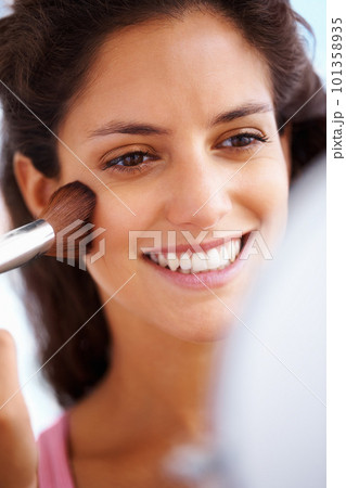 Beauty, grooming and makeup with woman apply blush to her face, happy and looking in a mirror at home. Young female excited to try skin cosmetics, smiling and getting ready, satisfied with results 101358935