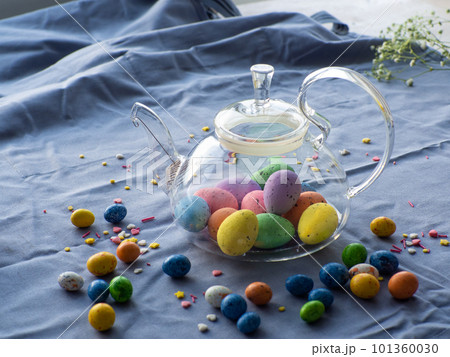 Easter eggs in glass teapot surrounded by small chocolate eggs and sprinkles Easter eggs in glass teapot surrounded by small chocolate eggs and sprinkles 101360030