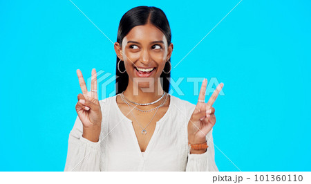 Happy woman, peace and face wink in studio, blue background and color backdrop. Portrait of female model, v sign and winking of cool girl for victory, smile and fun mood for happiness, emoji or hands 101360110
