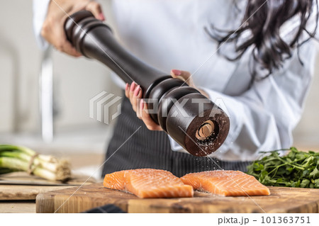 A salt grinder is used by a chef to season salmon in a restaurant kitchen 101363751