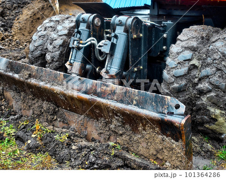 Wheeled tractor with shovel clears ground on cloudy rainy day. Dirty bulldozer shovel close-up.. 101364286
