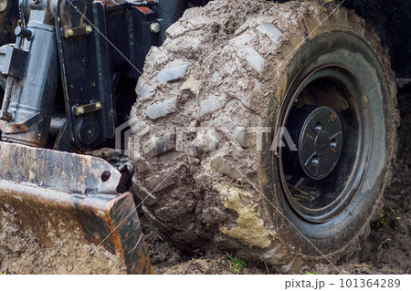 Wheeled tractor with shovel clears ground on cloudy rainy day. Dirty bulldozer shovel close-up.. 101364289