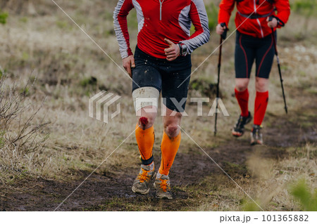 two runners run muddy trail sports race, knee is covered in blood injury from fall 101365882