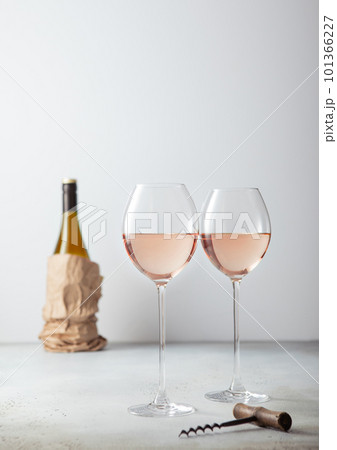 Pink rose glasses of wine with corkscrew and bottle on light board. 101366227