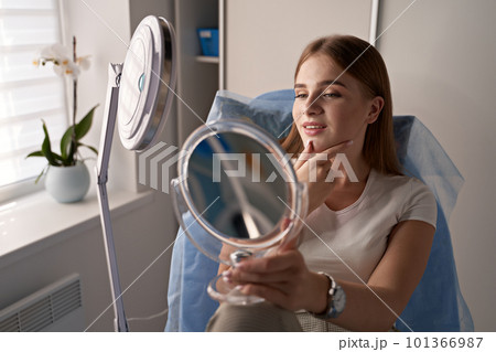 Young beautiful woman customer with mirror getting ready for beauty procedures in a medical salon 101366987