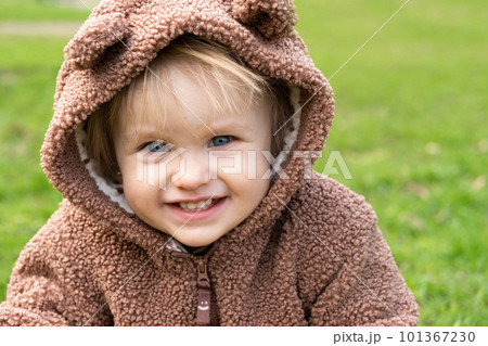 Portrait of a one-and-a-half-year-old blue-eyed girl in a bear costume in a park on the grass 101367230