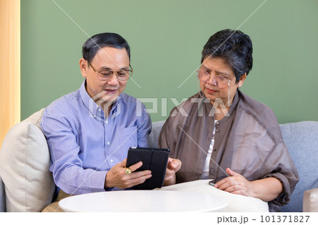 Asian retired elderly couple with eyeglasses, sitting on the sofa watching at tablet computer. 101371827