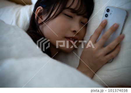 スマホを使いながら寝落ちする若い女性 スマホを使いながら寝落ちする若い女性 101374036