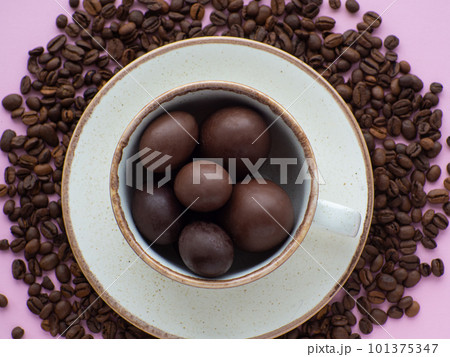 Mug full of chocolate eggs on plate with coffee beans on pink background 101375347