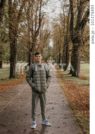 a guy in a jacket stands on an alley in the park during the fall season. Portrait oh handsome teen guy, young man in hoodie, down jacket standing, walking in beautiful golden autumn park, looking at a guy in a jacket stands on an alley in the park during the fall season. Portrait oh handsome teen guy, young man in hoodie, down jacket standing, walking in beautiful golden autumn park, looking at 101378895