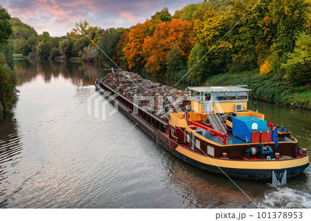 Transportation industry. Ship barge transports scrap metal and sand with gravel. Barge loaded with scrap metal is on the roadstead. Scrap metal transportation by water. Barge laden by metal salvage 101378953