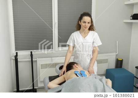 Female Doctor, Physician Sets Wireless Electric Muscle Stimulator On Back Of Disabled Child With Cerebral Palsy. Massage, Rehabilitation. Children with disability, special needs. Horizontal plane 101380021