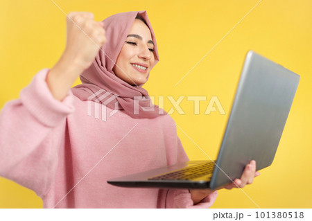 Happy muslim woman celebrating while using a laptop Happy muslim woman celebrating while using a laptop 101380518