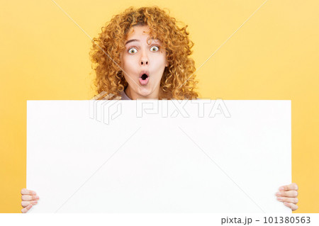 Surprised woman with curly hair holding a blank panel Surprised woman with curly hair holding a blank panel 101380563