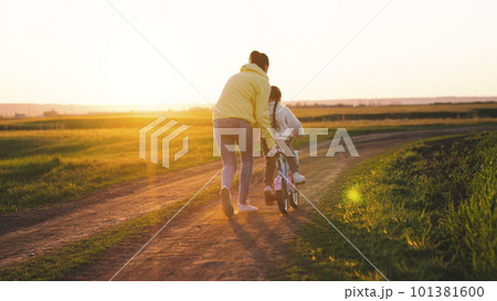 mother rides child bicycle sunset. happy family park. Mom teaches her daughter ride bike. concept happy family summer park. fun vacation. teamwork. mother runs green grass rolling child bicycle mother rides child bicycle sunset. happy family park. Mom teaches her daughter ride bike. concept happy family summer park. fun vacation. teamwork. mother runs green grass rolling child bicycle 101381600