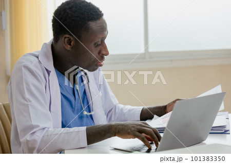 African American man doctor using laptop and paperwork checking report at table office hospital. 101383350