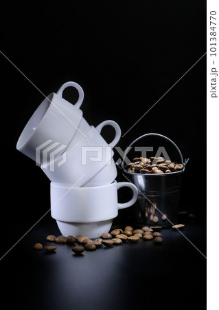 White coffee cups and roasted coffee in a bucket on a dark background in the studio. Coffee concept White coffee cups and roasted coffee in a bucket on a dark background in the studio. Coffee concept 101384770