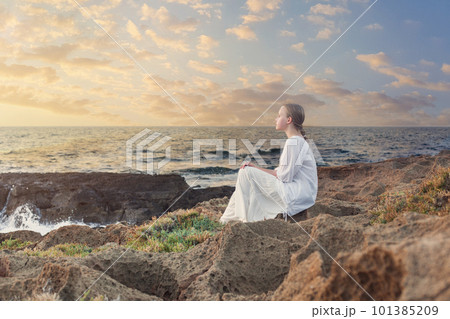 Teenage girl sitting on rocks near blue sea 101385209