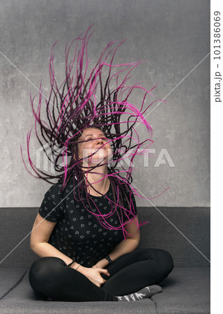 Happy woman waves her dreads with long violet dreadlocks sitting on sofa. Vertical frame. Stylish girl 101386069