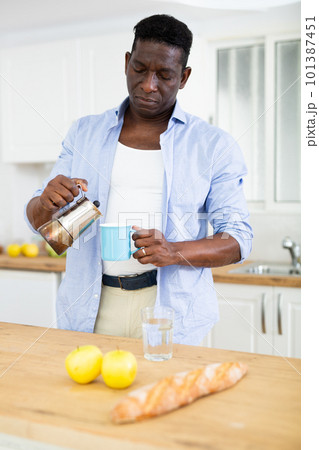 African american man pouring coffee from coffee pot for breakfast in kitchen 101387451