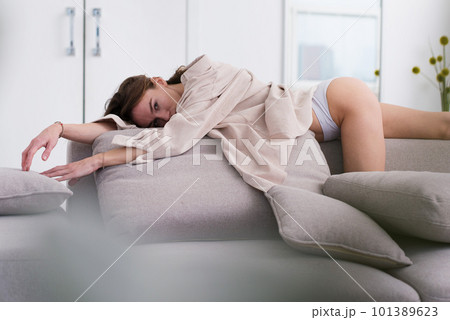 Woman in an unbuttoned shirt and underwear lies on the couch. 101389623